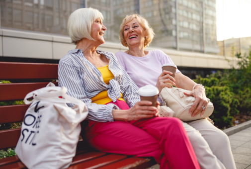 Two elderly women sat on a bench enjoying a coffee together and catching up